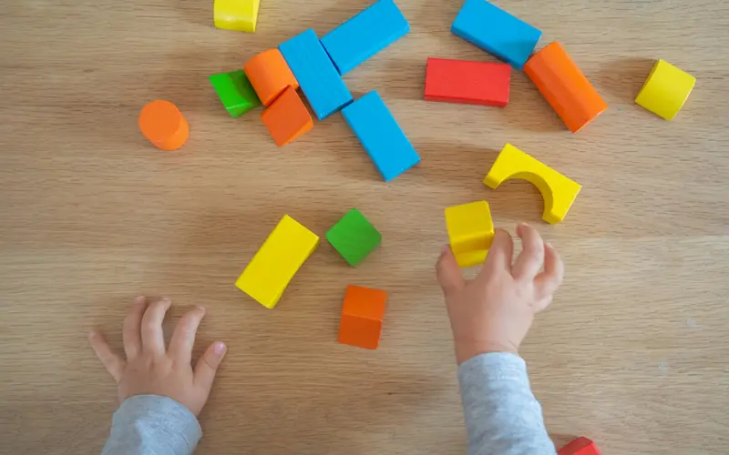 A young child's hands reaching for colourful wooden blocks on a wooden floor